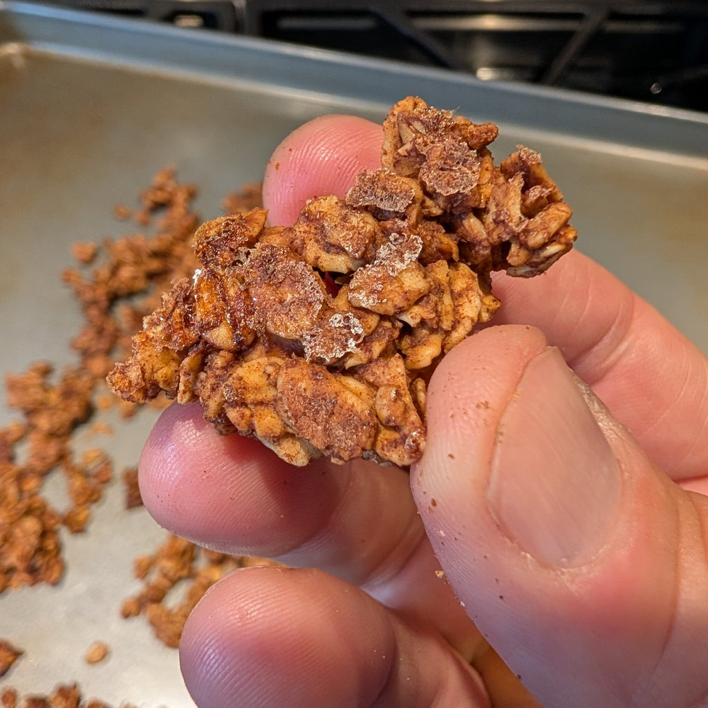 Hand holding a cluster of granola with a baking tray in the background
