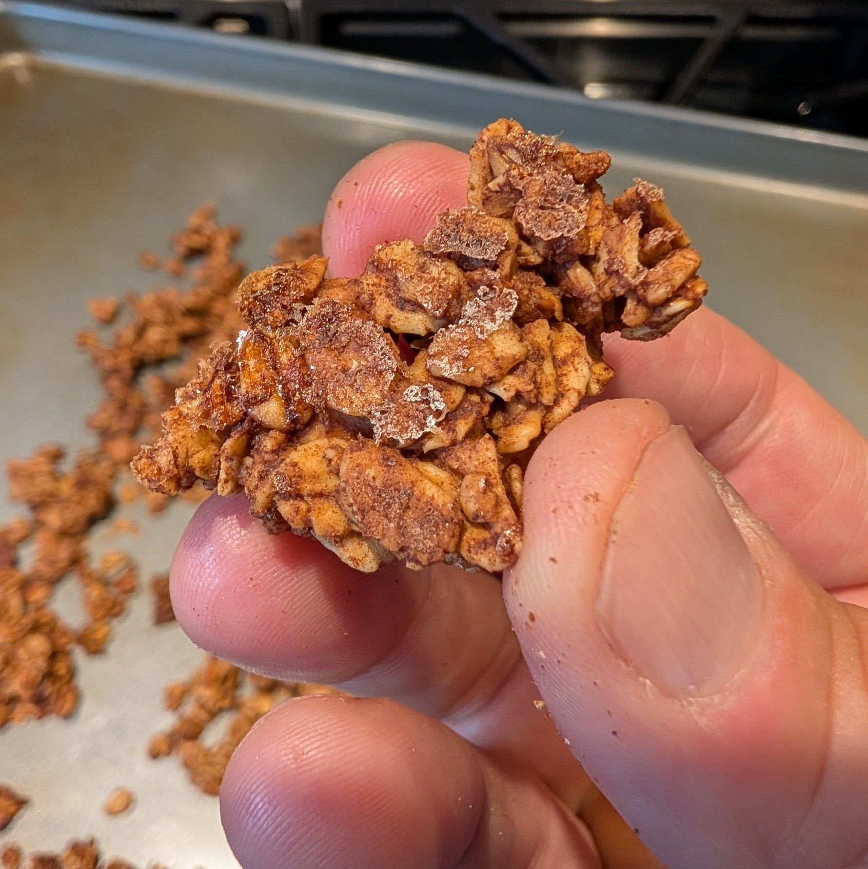 Hand holding a cluster of granola with a baking tray in the background
